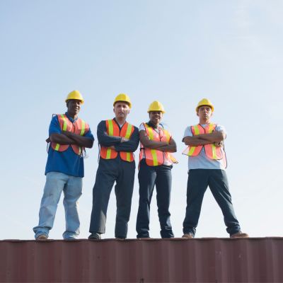 four construction workers standing on top of a building with the sky as background